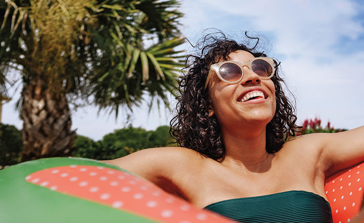 Woman with sunglasses on floating in a pool smiling