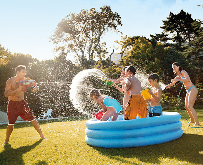 Kids standing in a portable inflatable pool while they play and splash water on adults standing outside of the pool