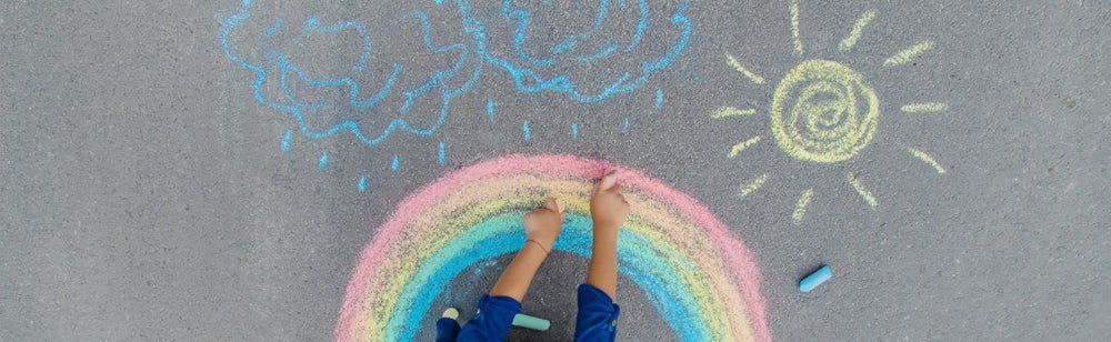 Picture of person using chalk on pavement to draw clouds, sun, and rainbow.