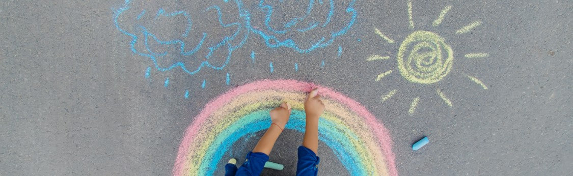 Picture of person using chalk on pavement to draw clouds, sun, and rainbow.